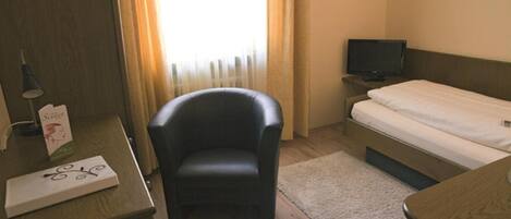 Habitación de hotel con escritorio de madera, sillón de cuero negro, cama, televisor y ventana con cortinas.