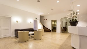 A modern lobby with a reception desk, seating area, and a staircase leading to upper floors. - Hotel Kurparkblick (Bad Bergzabern)