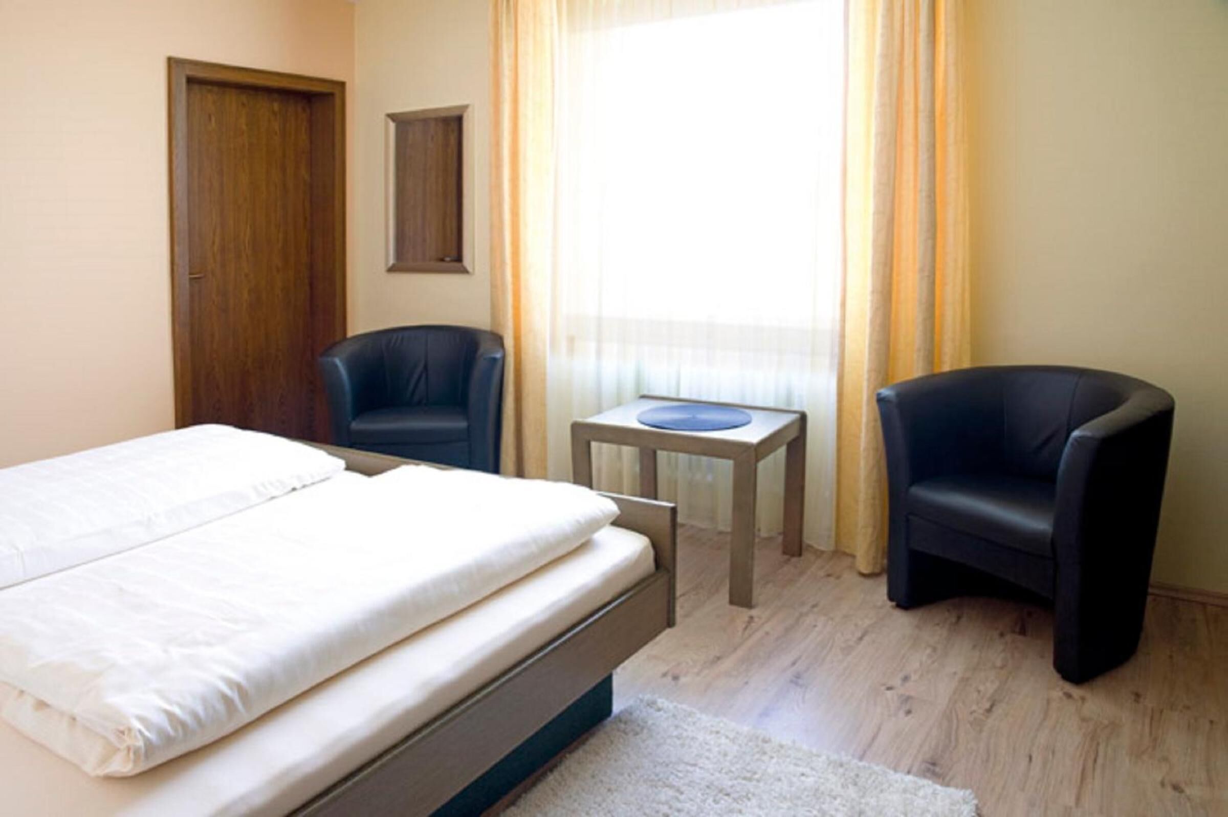 A hotel room with a bed, two chairs, a small table, and a window with curtains.