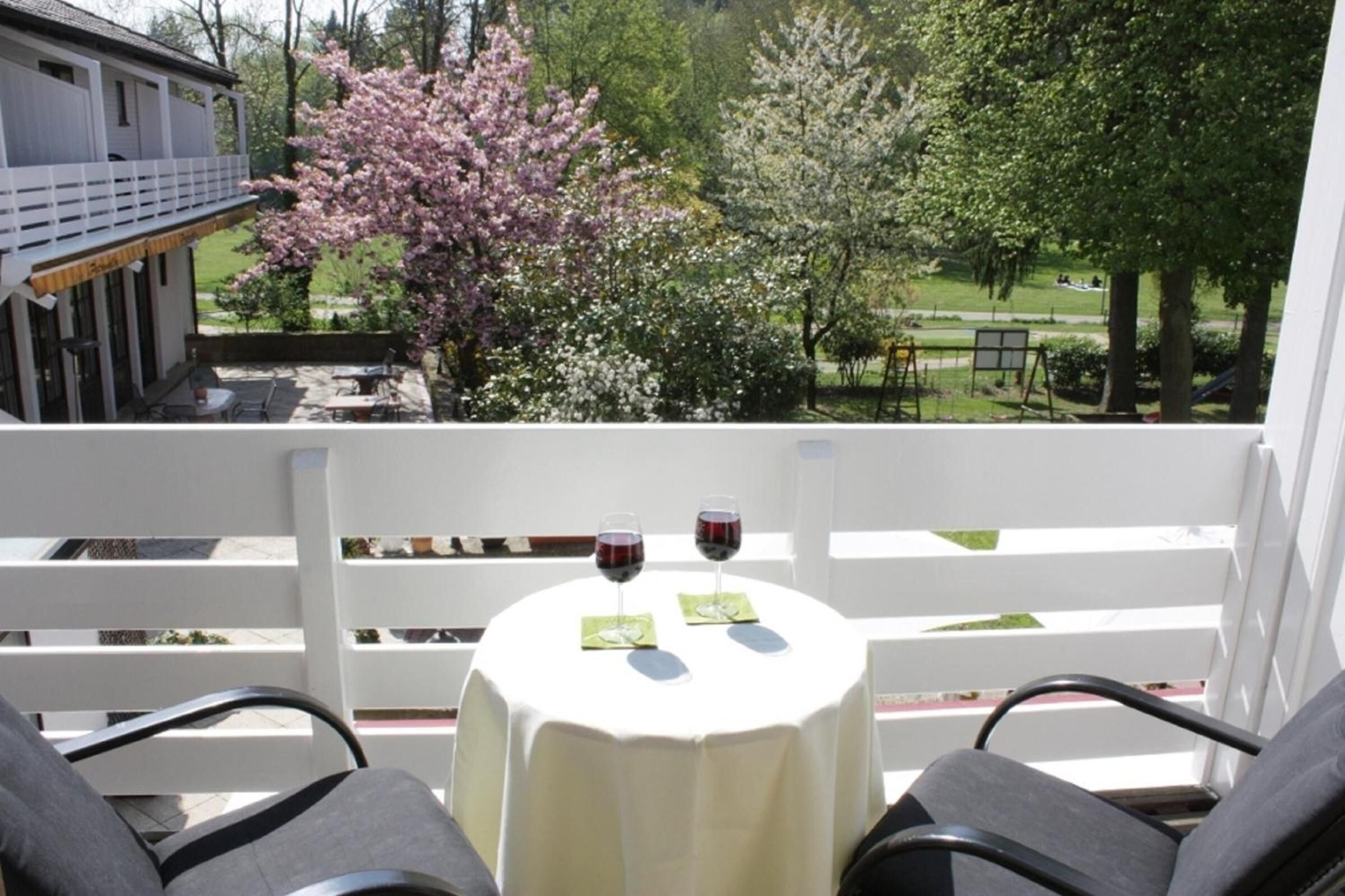 Ein Balkon mit Tisch für zwei Personen, mit Blick auf einen Garten mit blühenden Bäumen.