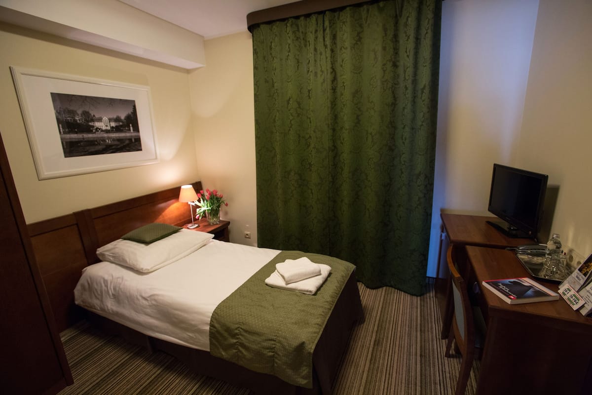 A hotel room with a neatly made bed, a television on a wooden table, and a framed picture on the wall.