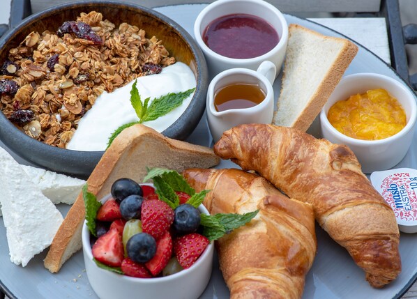 A breakfast tray with croissants, yogurt, granola, strawberries, blueberries, toast, jam, honey, and a cup of tea.