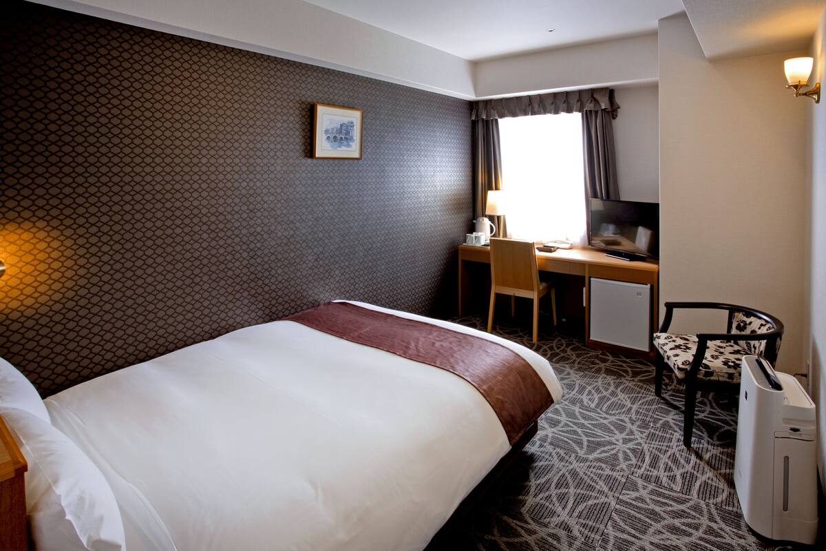 Een hotelkamer met een groot bed, een bureau, een stoel en een kleine kitchenette.