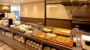 Una mesa de buffet con diversos alimentos y bebidas, un muro de ladrillo y una zona de cocina moderna.