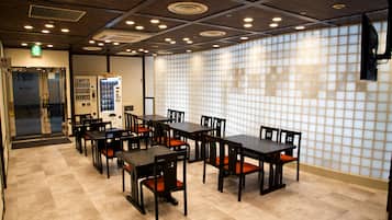 A restaurant with multiple tables and chairs, a vending machine, and a tiled wall.