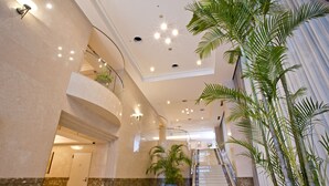 Un hall espacioso con suelo de mármol, una escalera y grandes plantas en macetas.