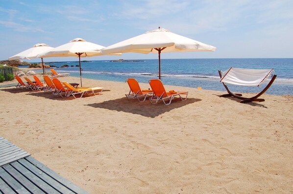 Una playa con sillas reclinables anaranjadas y sombrillas blancas.