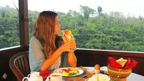 Una persona sentada a una mesa con comida y un vaso de jugo, con vistas a un bosque frondoso.