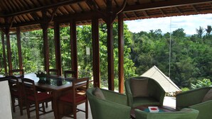 Un espacio cubierto al aire libre para comer, con una mesa y sillas, que da a un exuberante paisaje verde.