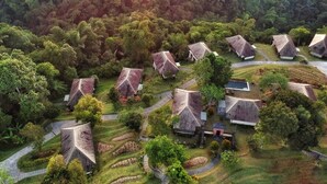 Vista aérea de un complejo turístico con varias cabañas de techo de paja rodeadas de exuberante vegetación y campos en terrazas.