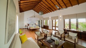 A spacious room with a high ceiling, wooden beams, a large bed, a dining table, and multiple chairs. - Aavya Cove Villas By Aahaasa (Balapitiya)