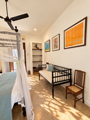 Ein Schlafzimmer mit einem Bett, einer Schlafcouch, einem Sessel, einem Deckenventilator und Kunstwerken an der Wand.