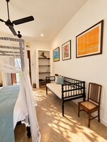 Un dormitorio con cama, una chaise longue, una silla, un ventilador de techo y obras de arte en la pared.