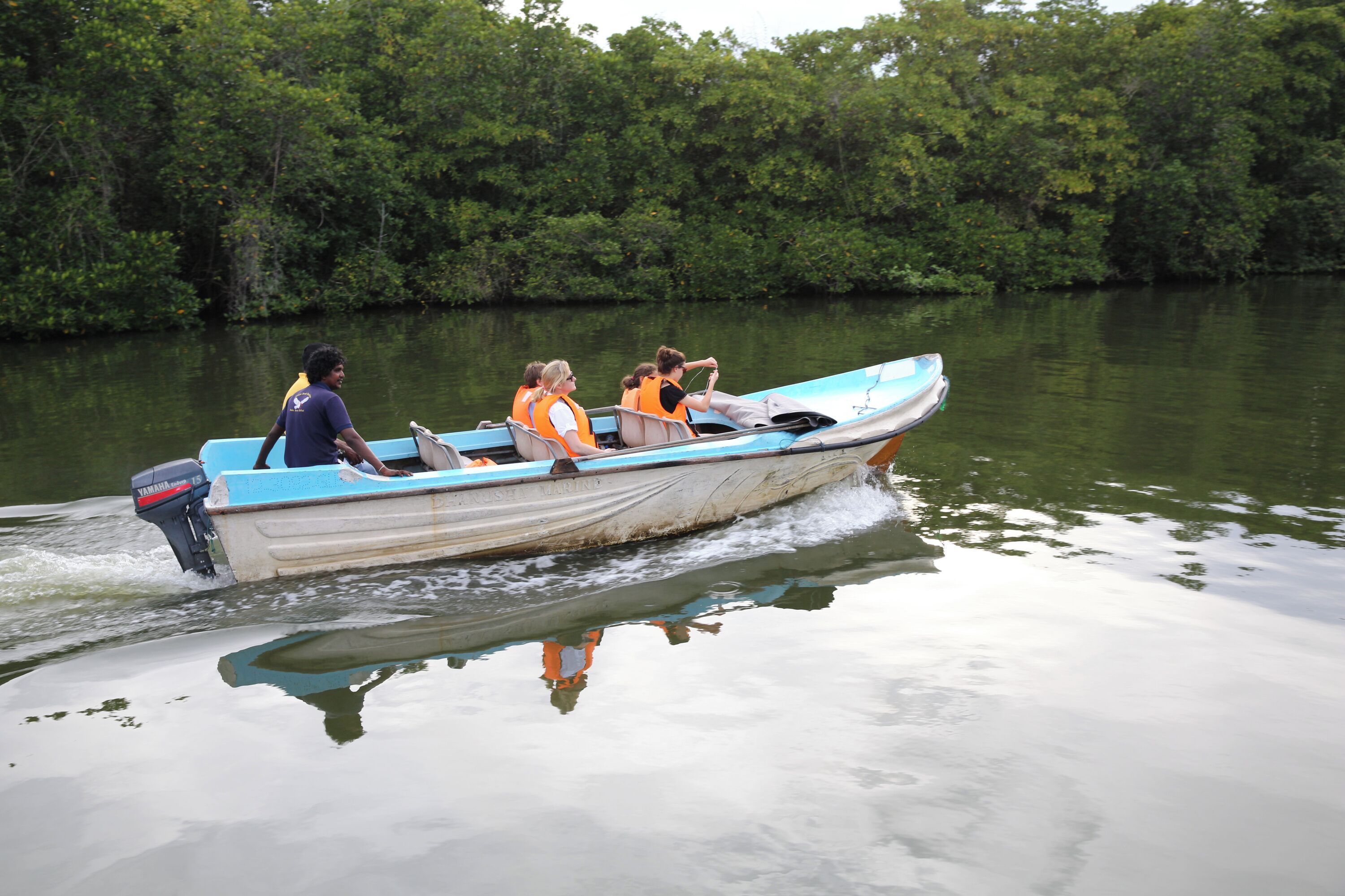 A small boat with four people wearing life jackets, moving through calm water surrounded by dense greenery.