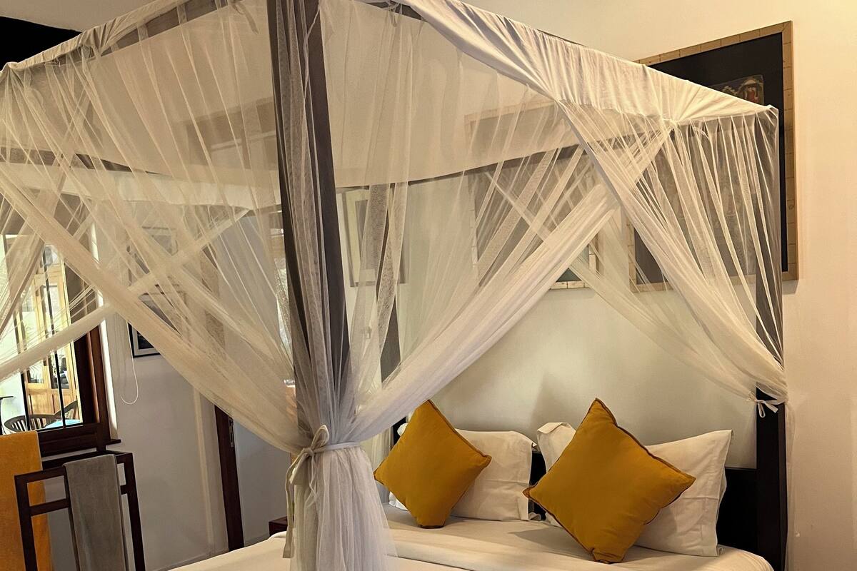 A bed with a canopy, white bedding, and two mustard-colored pillows.