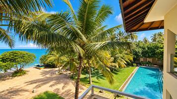 Vista de la piscina con una clara vista del océano, una palmera y un pequeño bote.