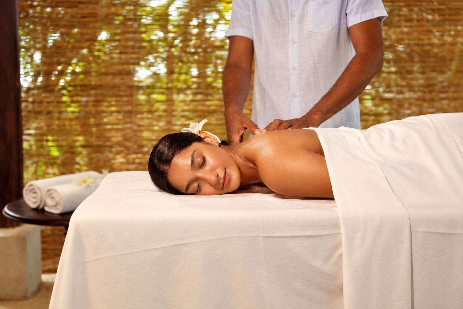 A person receiving a massage in a room with a bamboo backdrop.