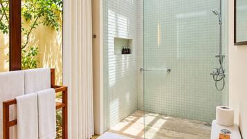 Un baño con ducha envuelta en vidrio, inodoro y toallero con toallas.