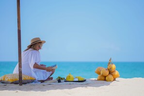A person sitting on a beach with a picnic setup including a yellow teapot, cups, and a plate of food. - Aavya Cove Villas By Aahaasa (Balapitiya)