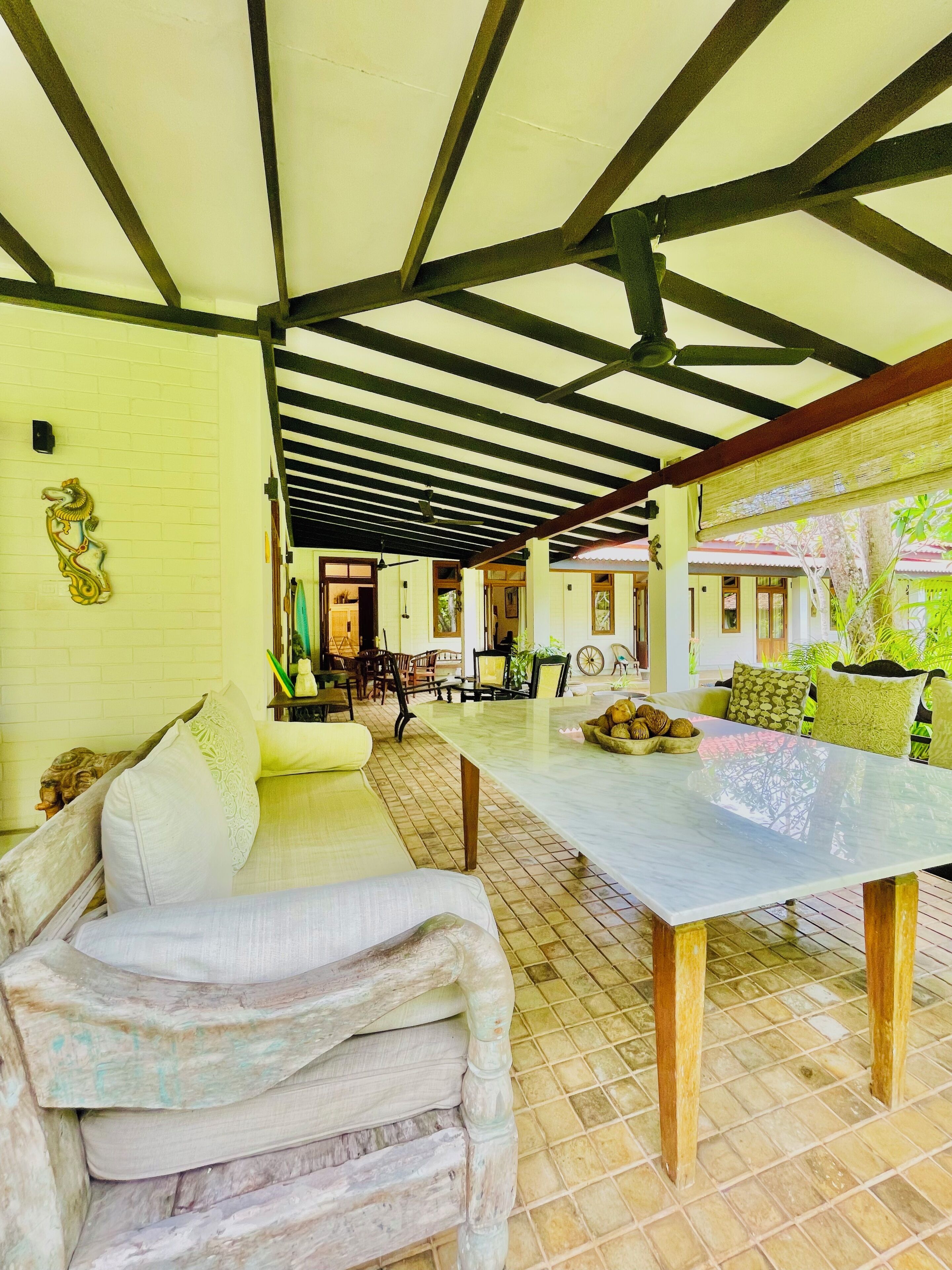 A covered outdoor seating area with a table and chairs, a sofa, and a decorative wall piece.