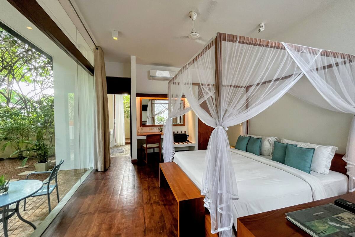 A bedroom with a canopy bed, a desk, and a view of the outdoors.