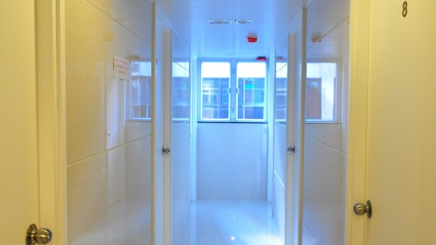 A hallway with white walls and doors, leading to a room with a window.