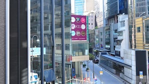 A modern urban street with high-rise buildings, a construction site with scaffolding, and a pedestrian crossing.