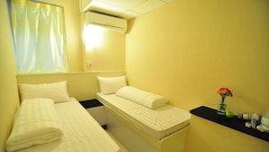 A small, yellow-walled room with two beds, a small table with a vase of flowers, and an air conditioning unit.