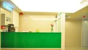 A reception desk with a green counter, an exit sign, a small plant, and a vase with flowers.