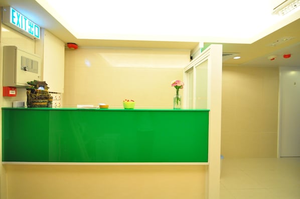 A reception desk with a green counter, an exit sign, a small plant, and a vase with flowers.