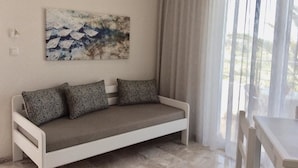 Un salon moderne avec un canapé blanc, un tableau accroché au mur et une vue dégagée sur l’extérieur grâce à une grande fenêtre.