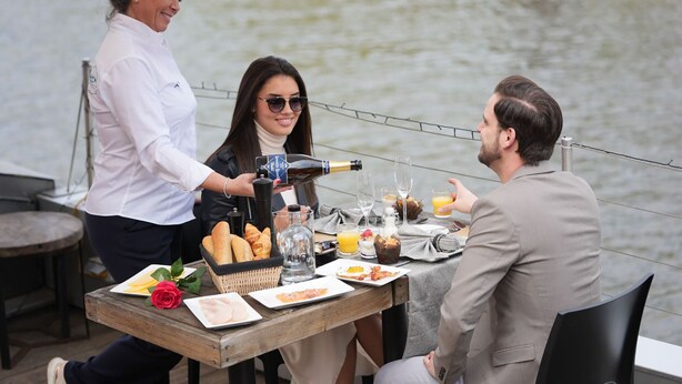 A table set for a meal by a waterfront with a bottle of champagne, bread, and various dishes. - Hotel Restaurant Brasserie Ahoi, Kortrijk (Kortrijk)