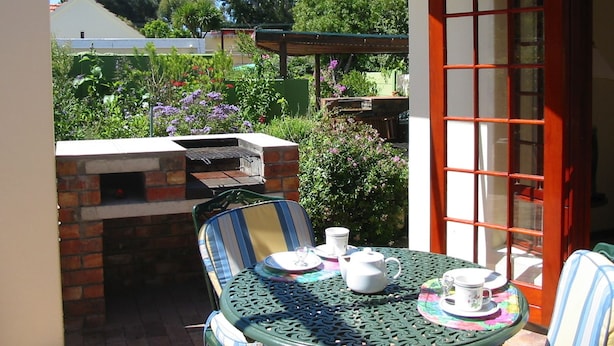 Une terrasse avec un barbecue en briques, une table dressée avec des tasses et des soucoupes à thé, et une chaise.