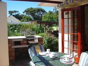 A patio with a brick barbecue, a table set with tea cups and saucers, and a chair. - Ascot Gardens Self Catering (Cape Town)