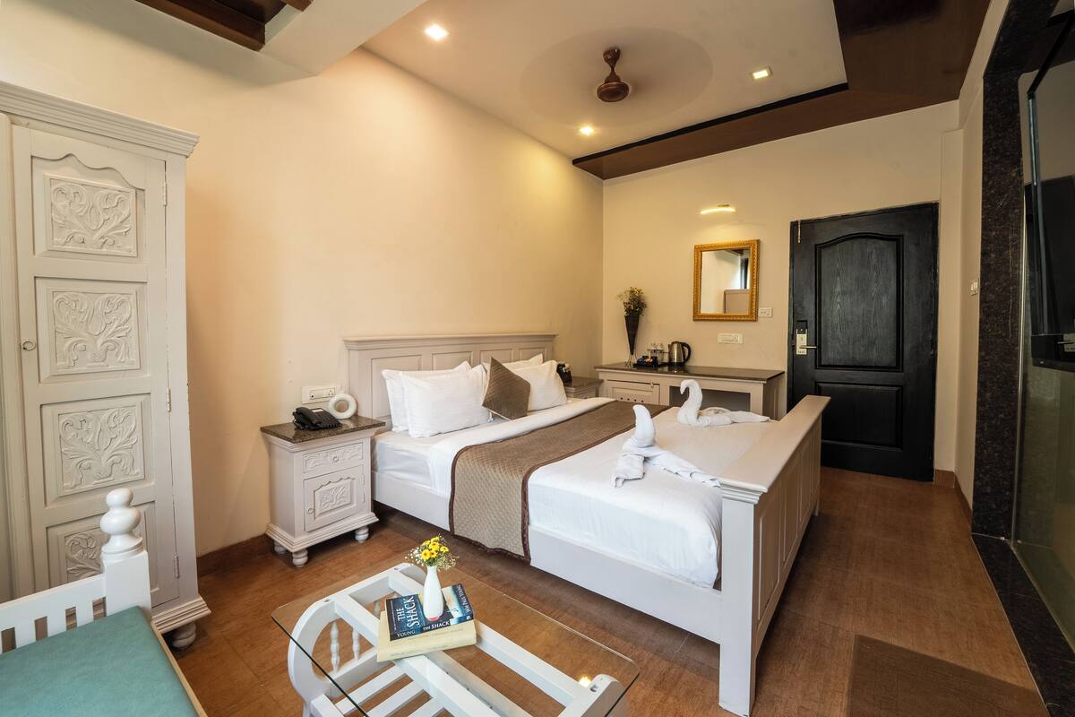 Habitación de hotel con una cama grande, una mesita de noche con lámpara, un aparador y un baño con ducha.