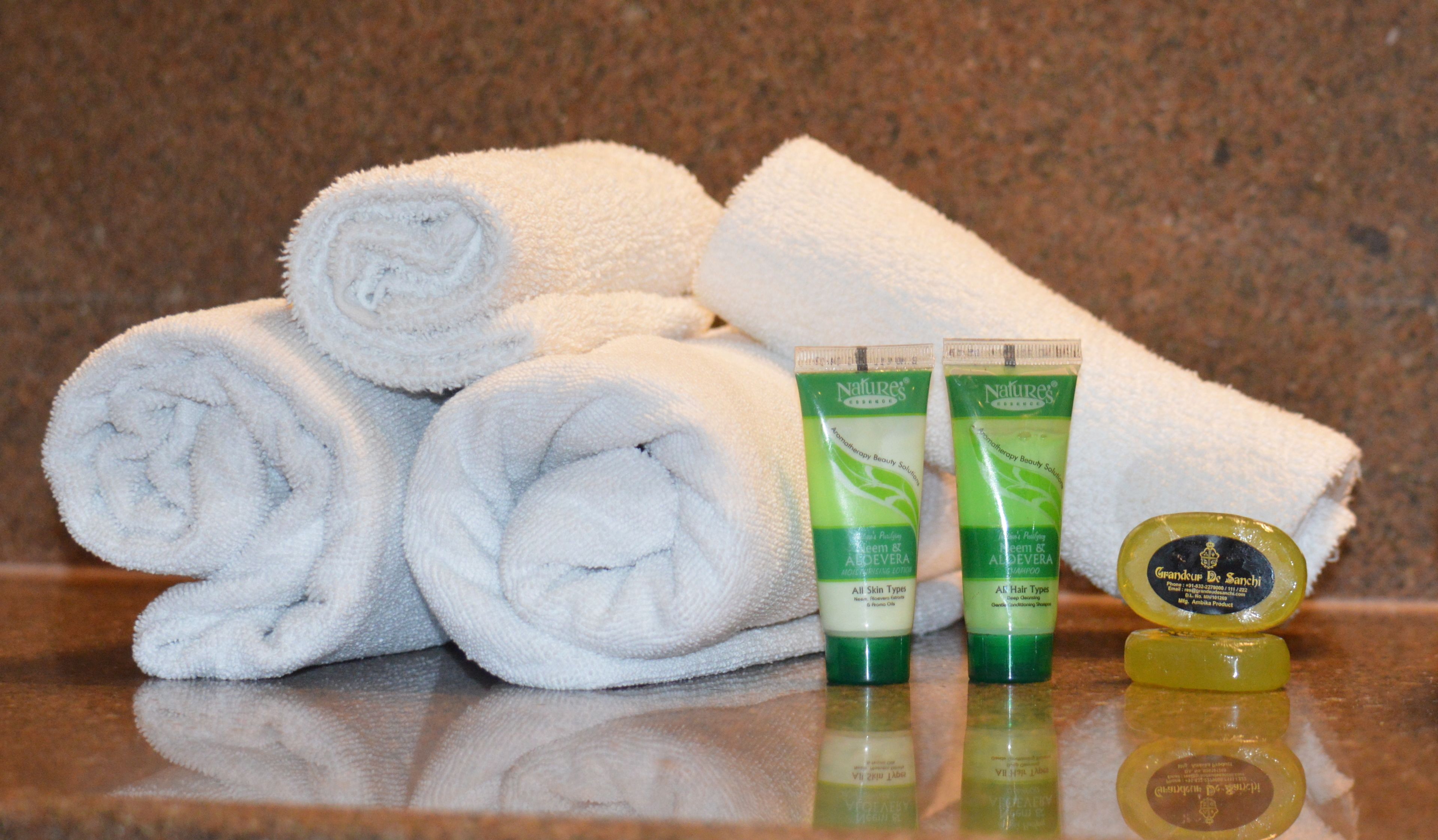 Neatly rolled white towels, two Nature's Beauty Aloe & Tea Tree Shampoo tubes, and a bottle of Grandoup De Sanchi.