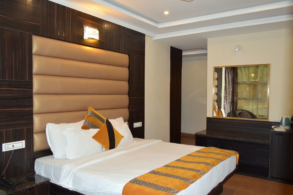 A hotel room with a large bed, a wooden headboard, a bedside table, a mirror, and a wardrobe.
