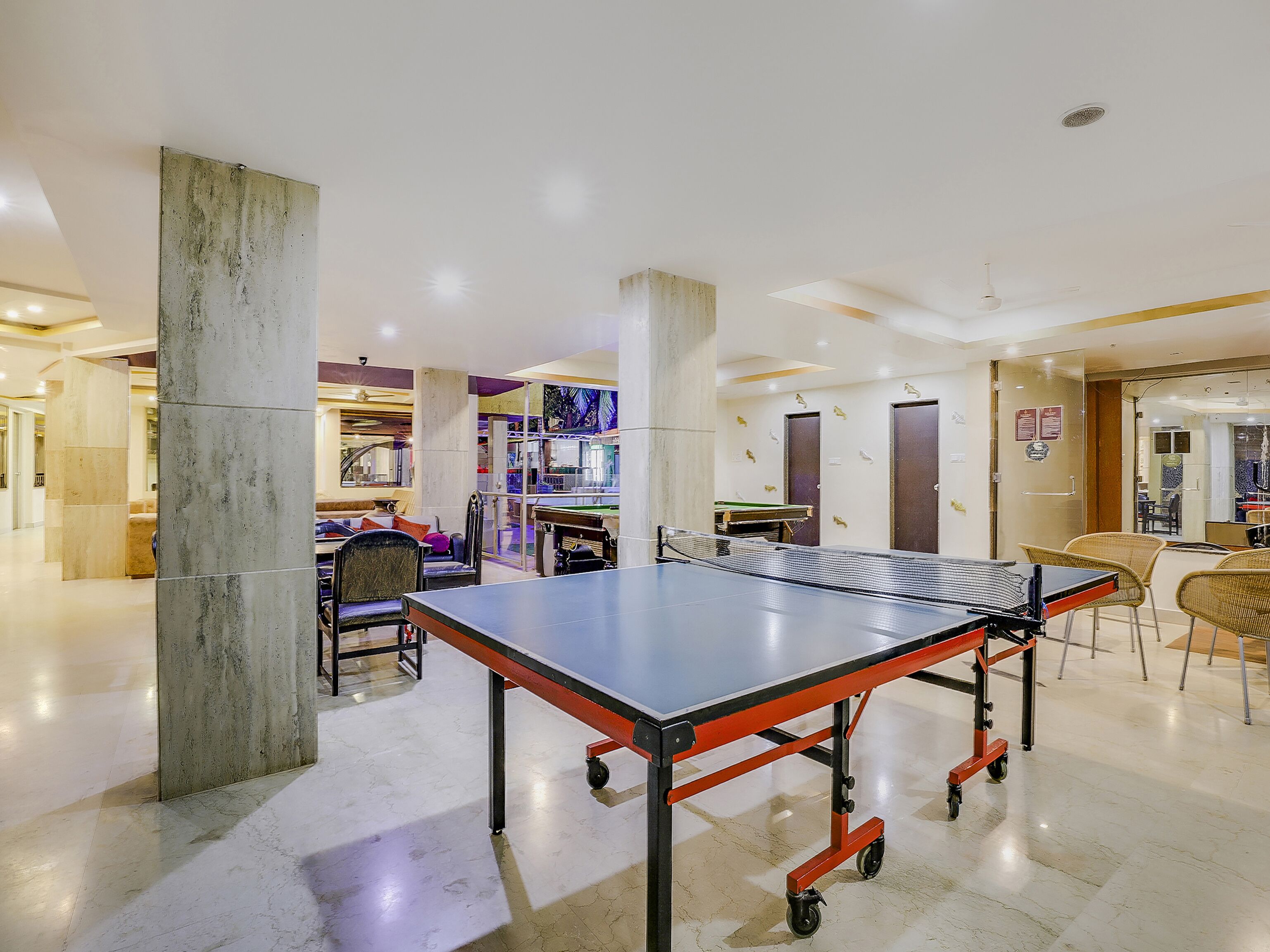 Una mesa de ping pong en un espacio interior bien iluminado con diseño moderno, que incluye un pilar grande y una partición de vidrio.