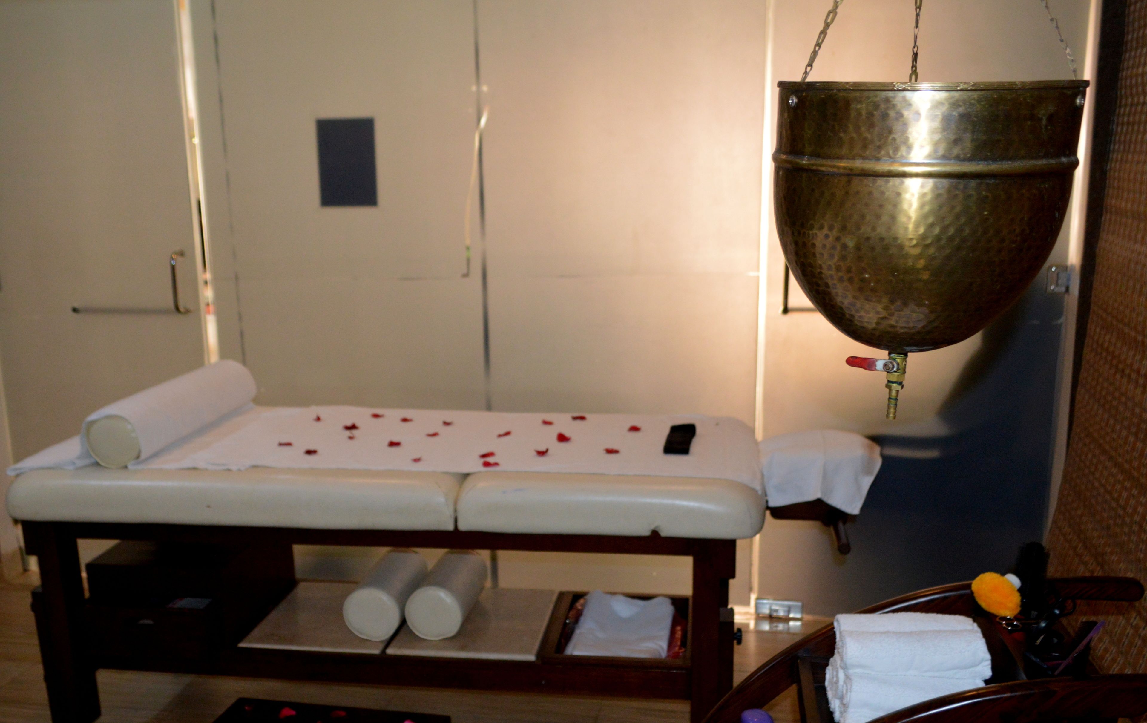 A massage table with a white sheet, two rolled-up towels, and a small tray with a towel and a bottle.