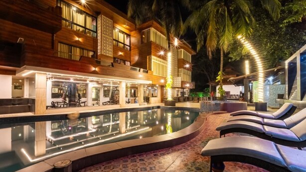 Un hotel moderno con piscina, sillas de descanso y un espacio exterior bien iluminado.