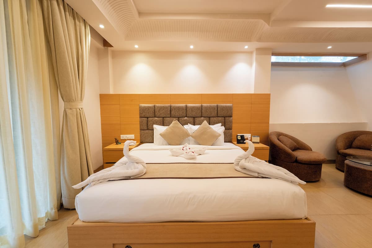 Una habitación de hotel moderna con una cama grande, cabecero de madera y dos sillones marrones.