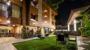 Un hotel moderno con un espacio exterior bien iluminado que incluye césped, mobiliario exterior y una piscina.