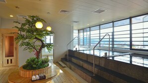A spa area with a wooden bench, a tree planter, and a view of the sea through large windows.