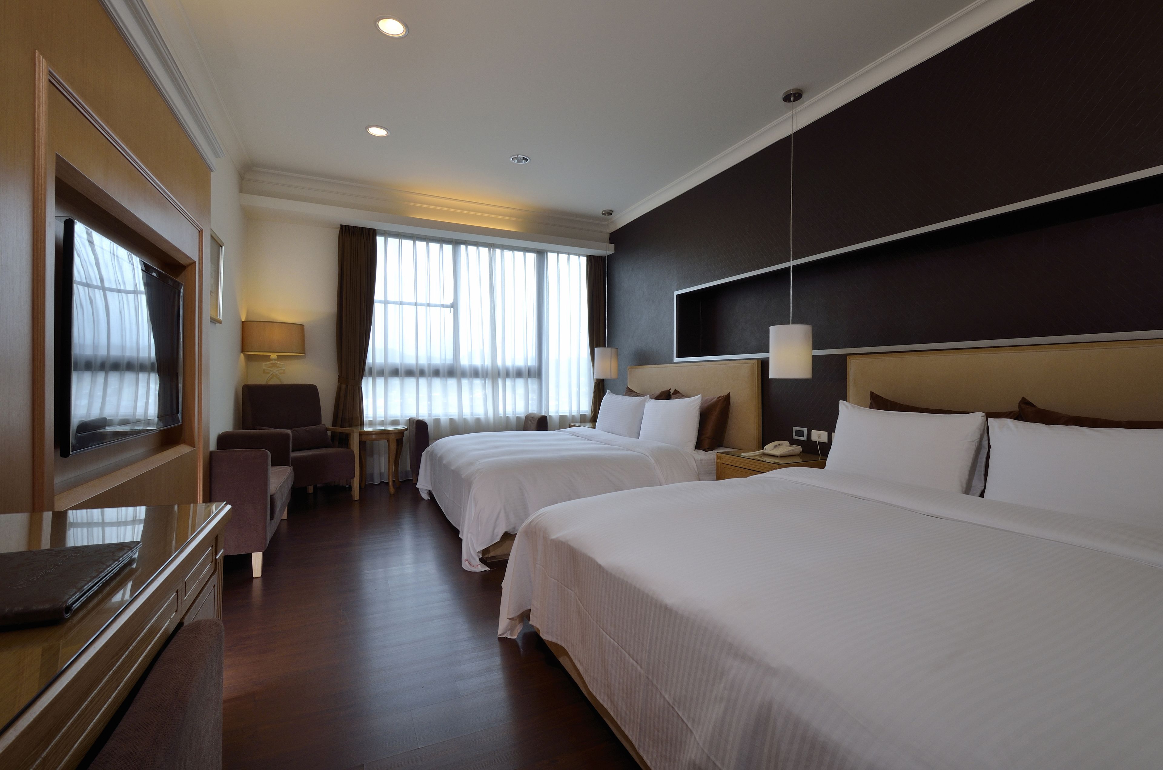 A hotel room with two beds, a desk, a chair, and a television.