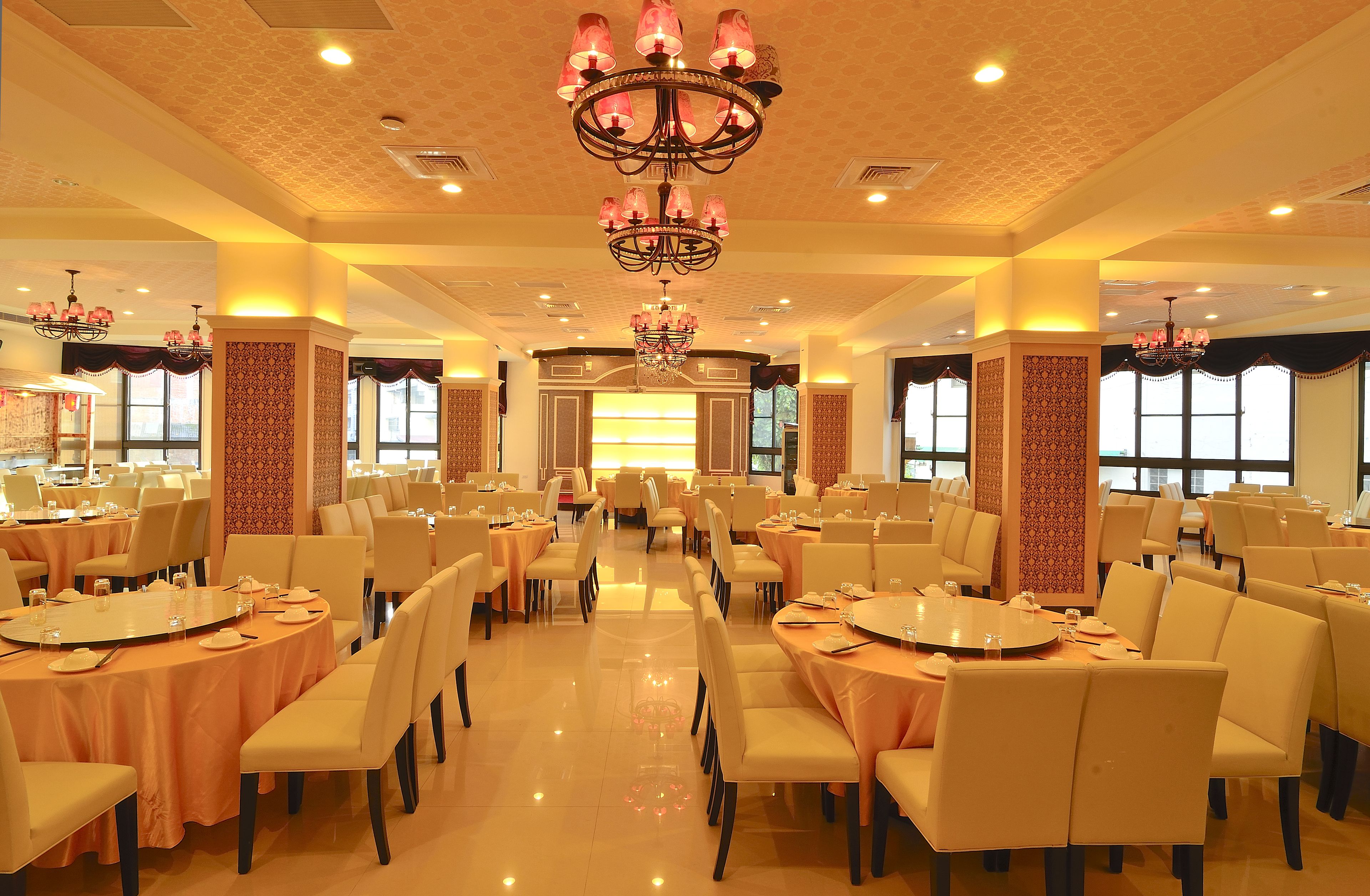 A spacious banquet hall with multiple round tables, chairs, and chandeliers.
