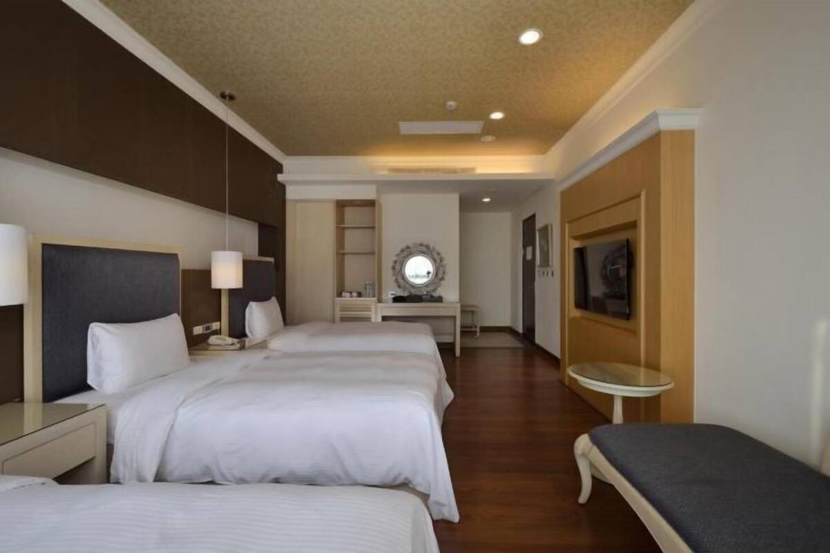 Une chambre d’hôtel avec deux lits, une petite table, un miroir et un téléviseur.