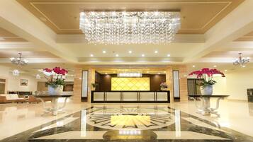 A spacious lobby with a large chandelier, a reception desk, and potted orchids.
