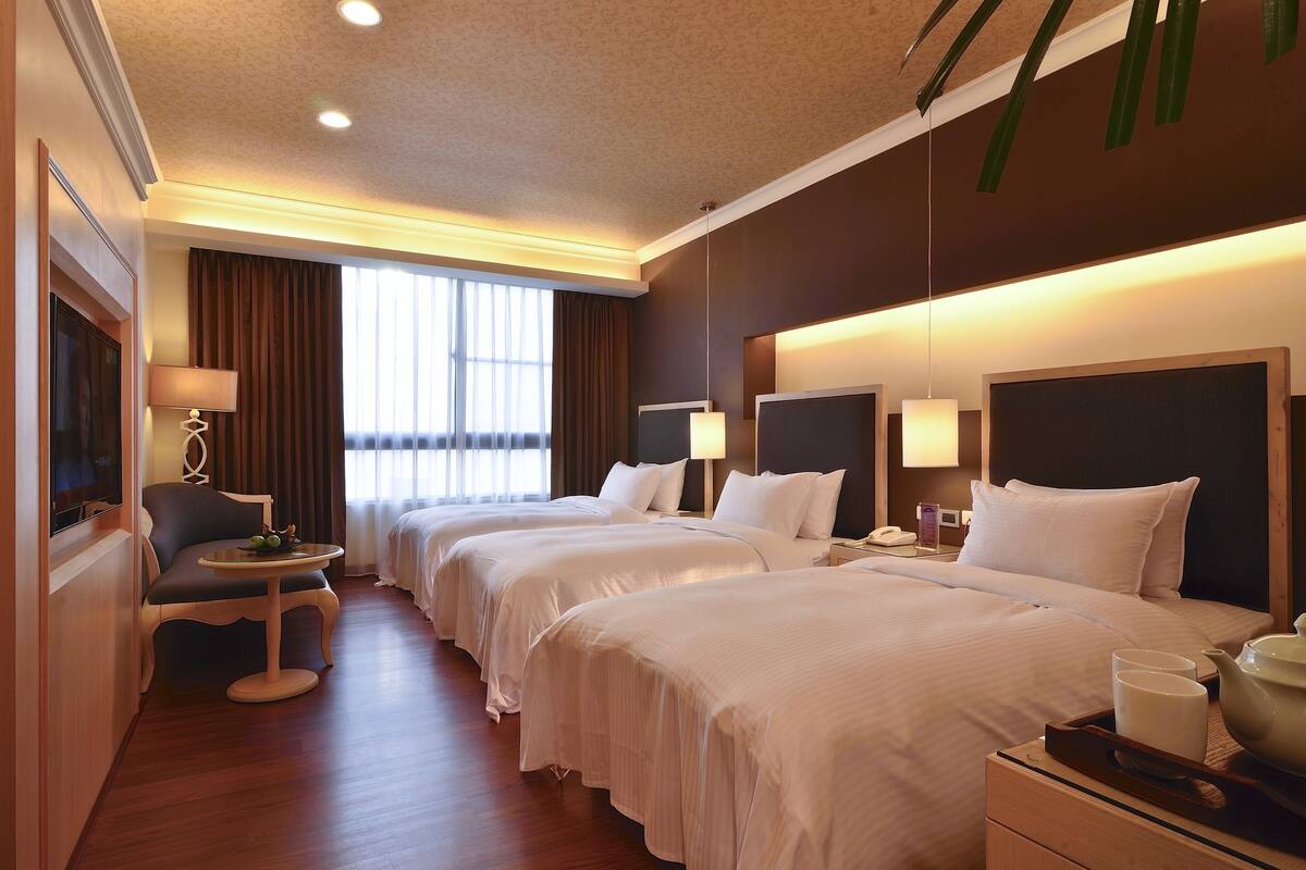 Une chambre d’hôtel avec deux lits, une petite table avec une lampe, une télévision et une fenêtre avec des rideaux.