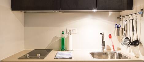 Una cocina con armarios de madera oscura, un lavamanos de acero inoxidable y una encimera con una tableta, una botella verde y una toalla blanca.