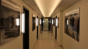 A hotel corridor with framed artwork on the walls, a tiled floor, and a ceiling light. - Getaway Leuven (Leuven)